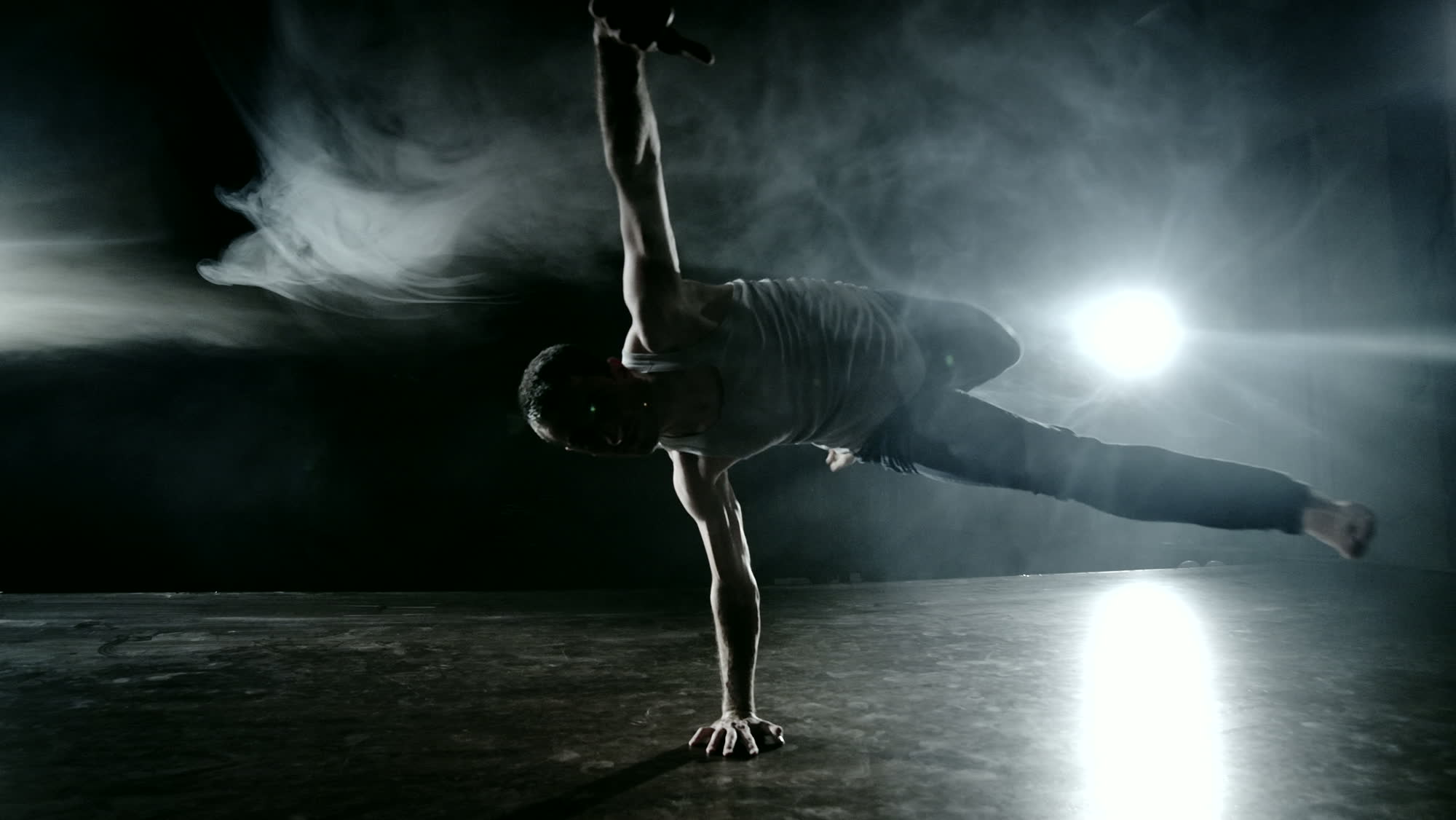 A dancer held horizontally in mid-air, supported on one hand, lit hard from behind through smoke.