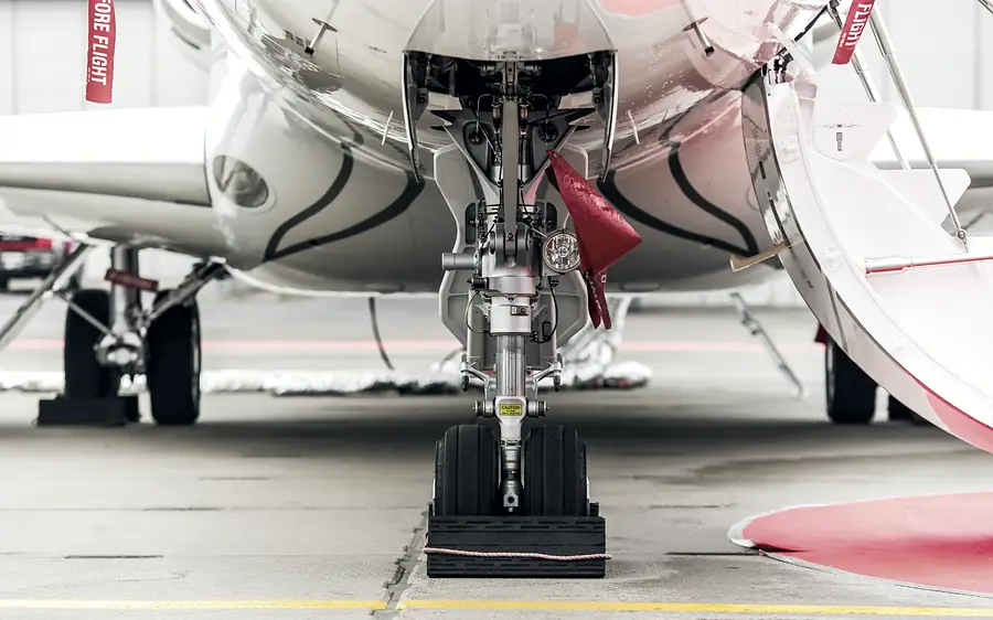 The nose gear of a business jet, a red streamer still on the pin, seen from the apron.