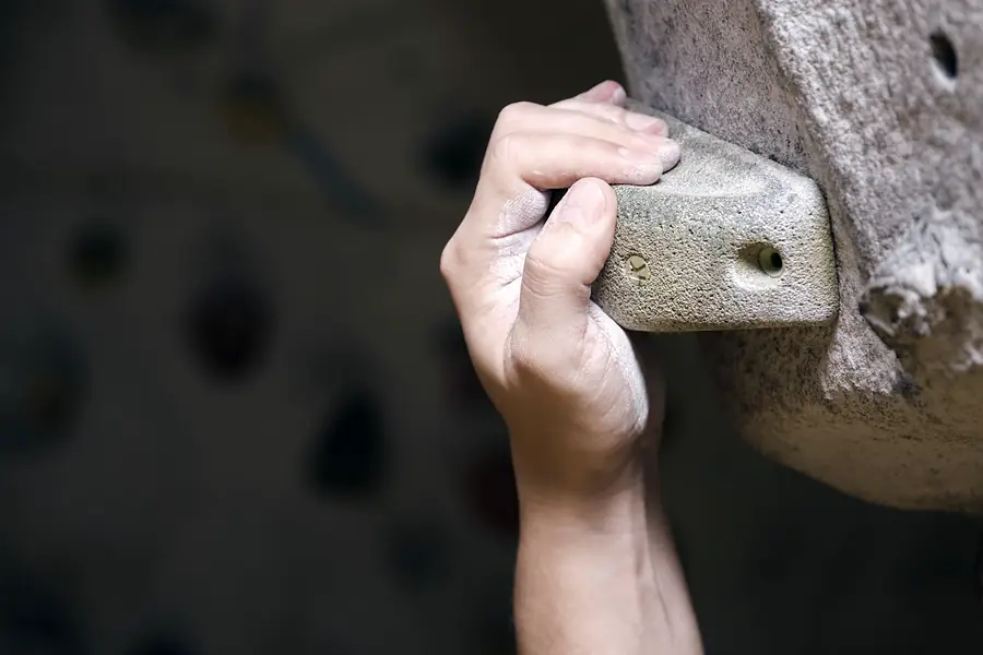 A chalked hand holding a climbing hold.