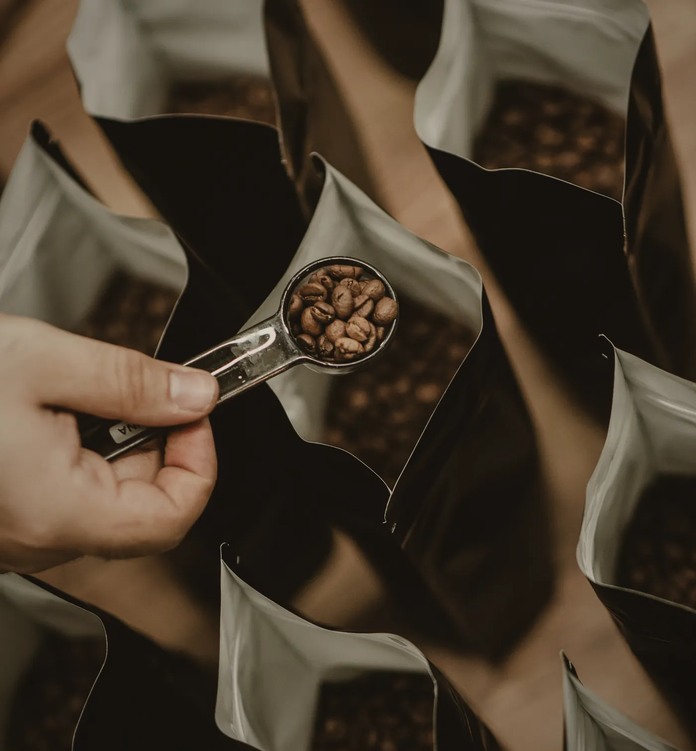 Looking down on a row of open foil valve bags as a steel scoop tips roasted beans into one of them.