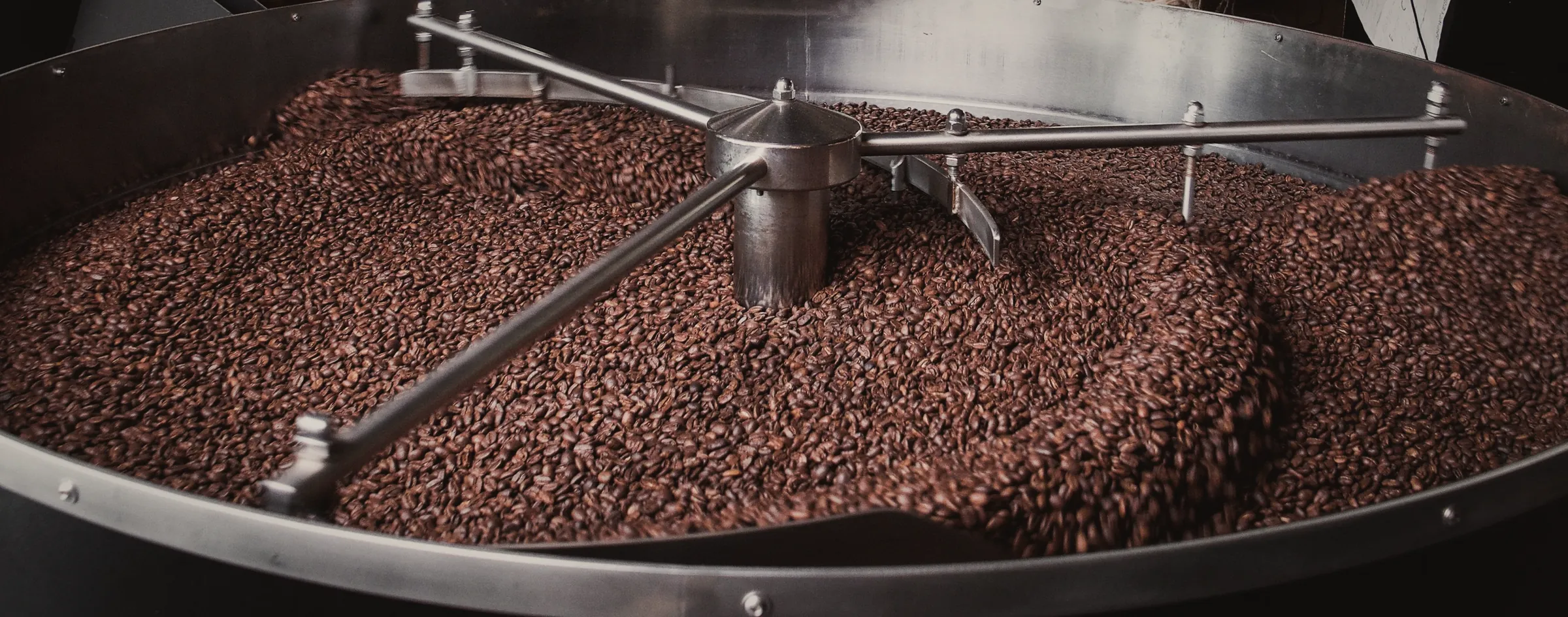 A steel cooling tray full of freshly roasted beans, stirring arms reaching across it.