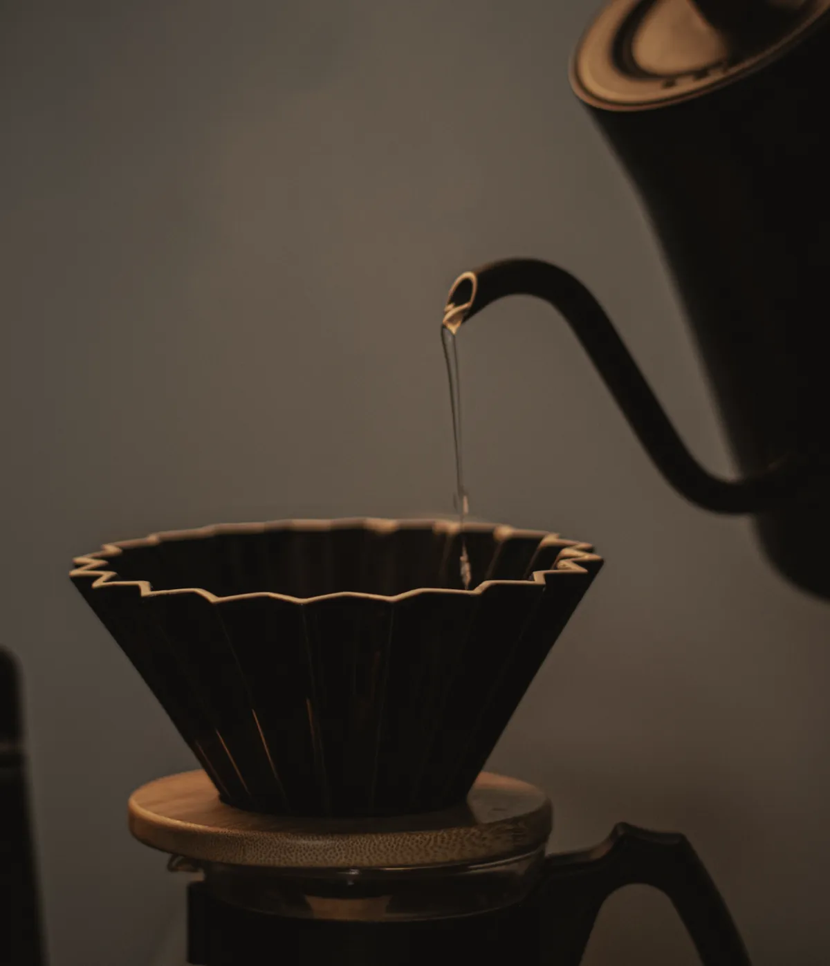 A black fluted dripper with a thin stream of water falling into it from a gooseneck kettle.