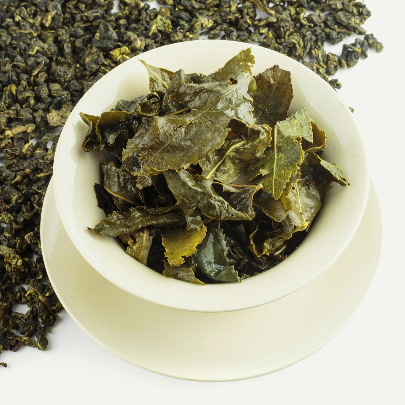 The same oolong before and after: a white bowl of opened leaves, broad, green and whole, with the dry rolled pellets scattered behind it.