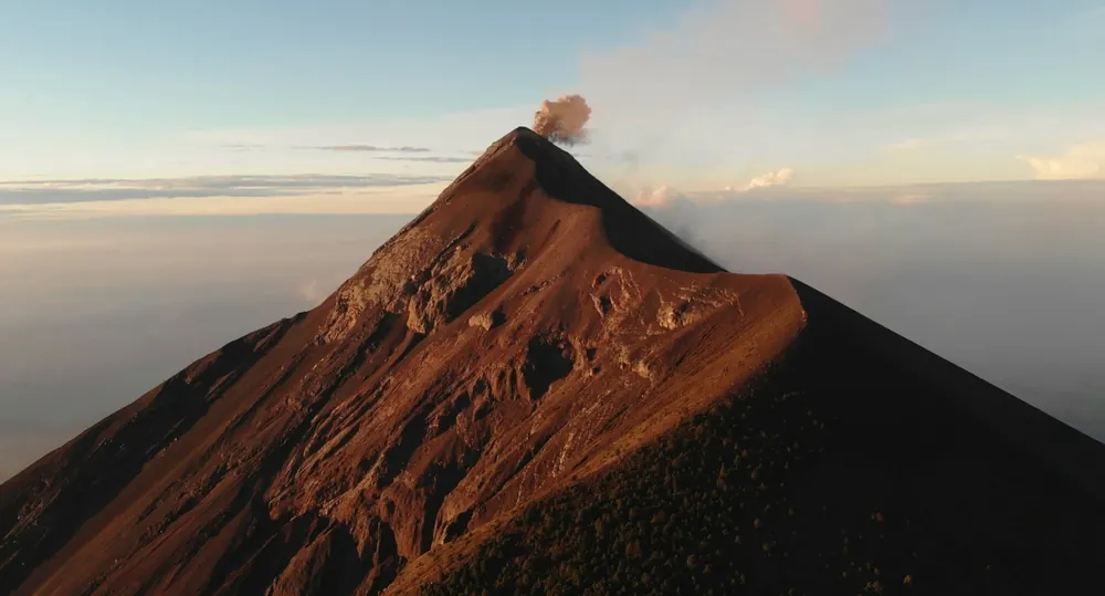 The upper cone of Volcán de Fuego, its flank lit a deep rust red, with a small plume of ash at the summit.