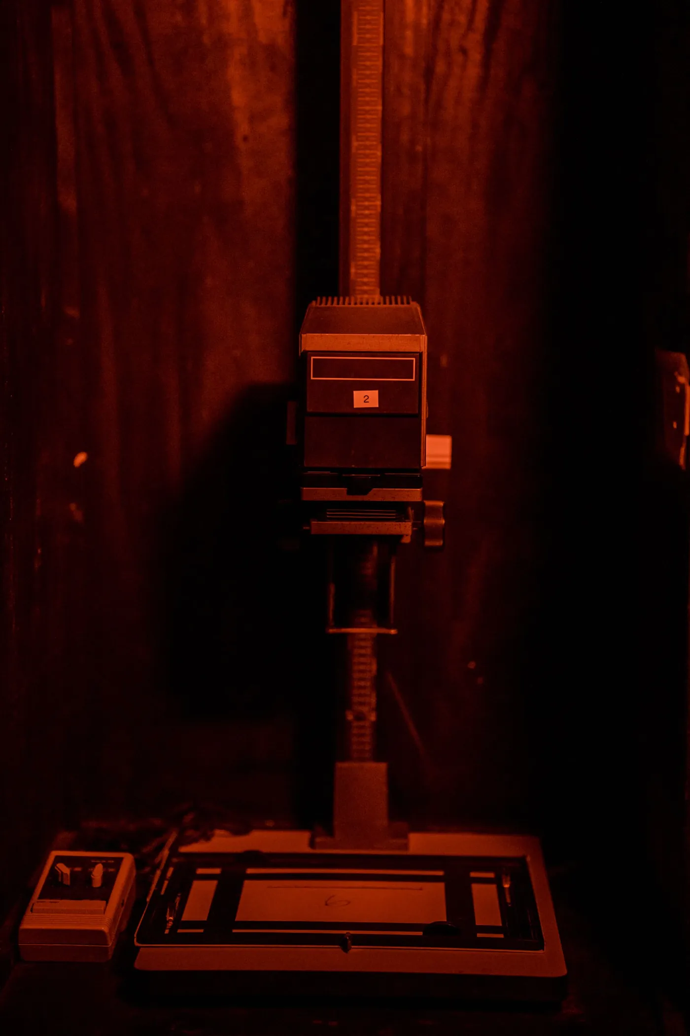 A condenser enlarger on its column under red light, the baseboard and easel below it.