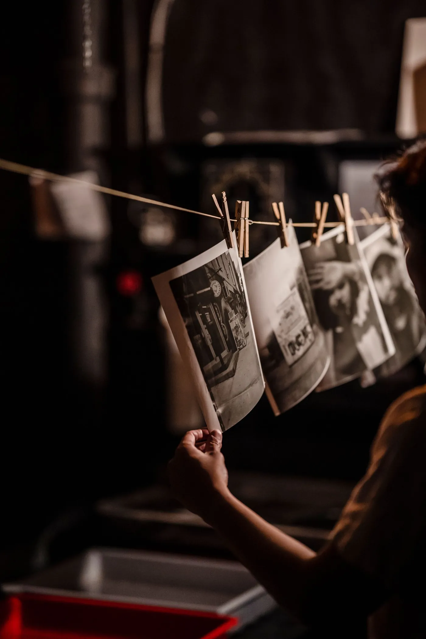 A printer reaching up to a line of black-and-white prints drying on pegs above the trays.