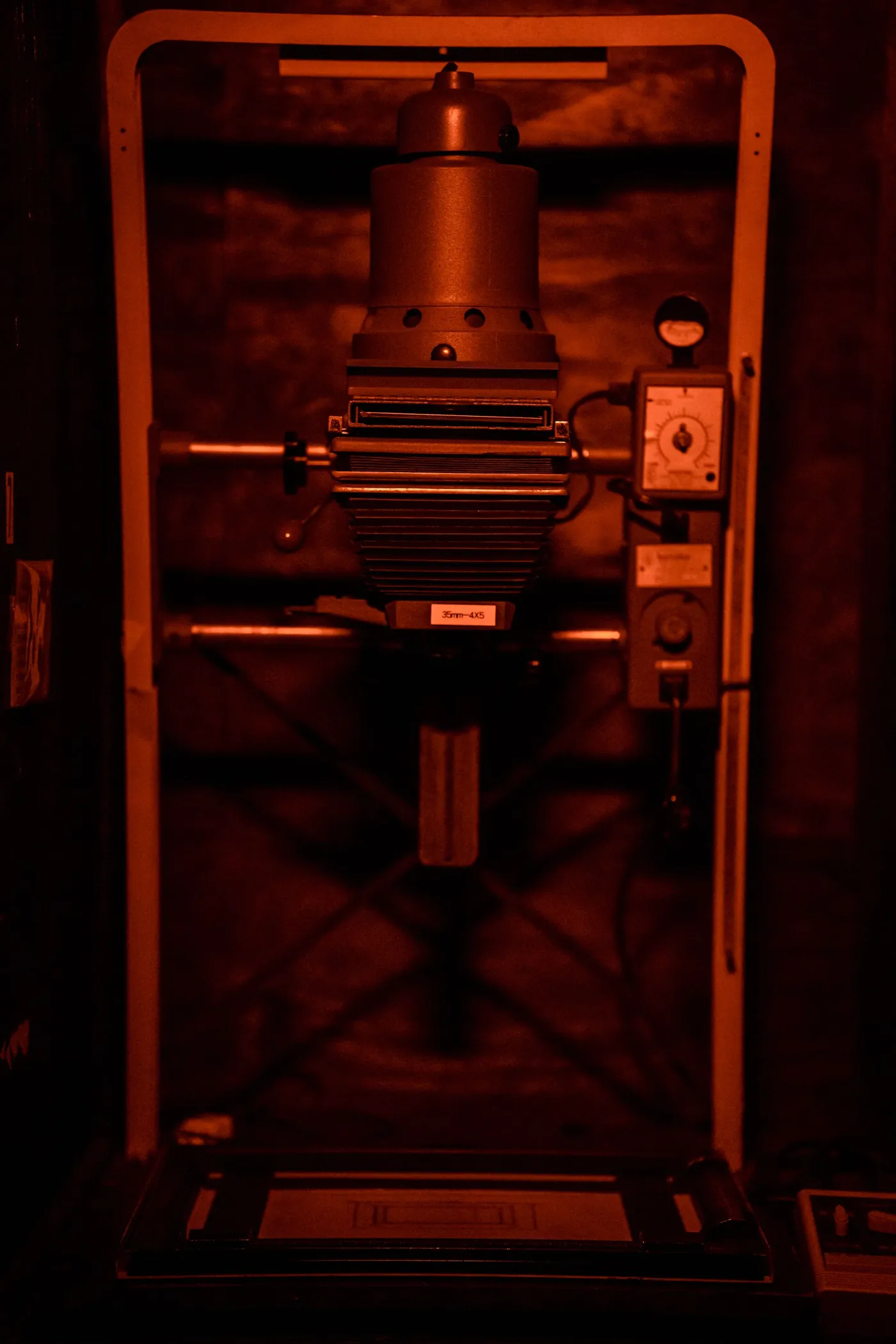 The head of an enlarger in its bay, the column and focus knob lit red.
