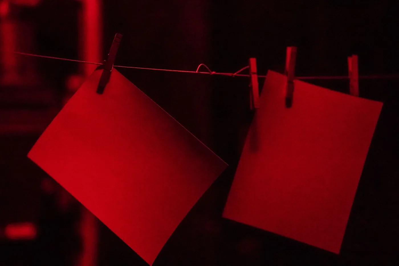 Two blank sheets of photographic paper pegged to a line under red safelight.