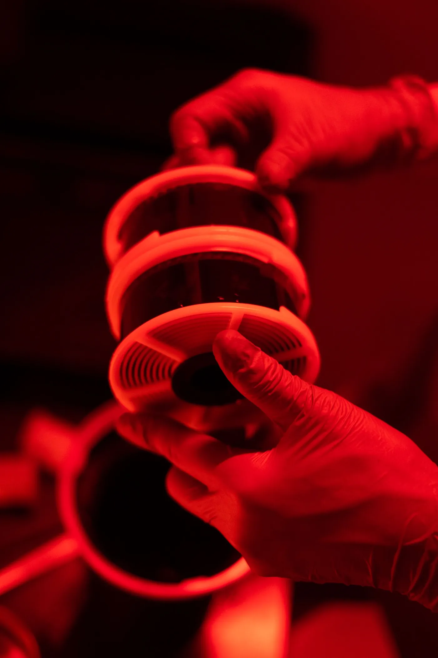 Gloved hands loading film onto a spiral reel under red light.