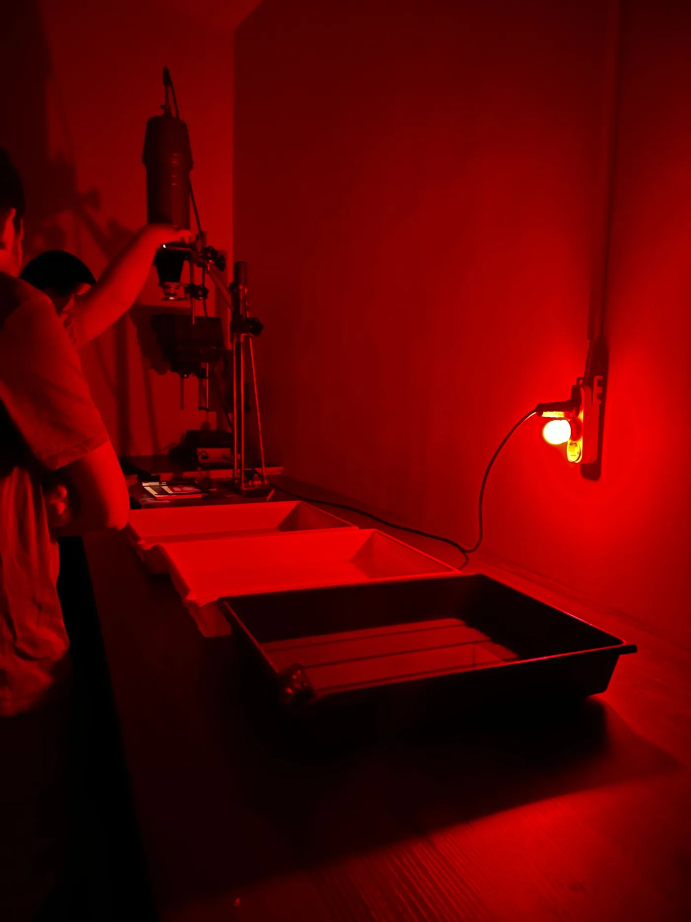 The wet side of the darkroom: a row of trays on a sink under a single red safelight on the wall.