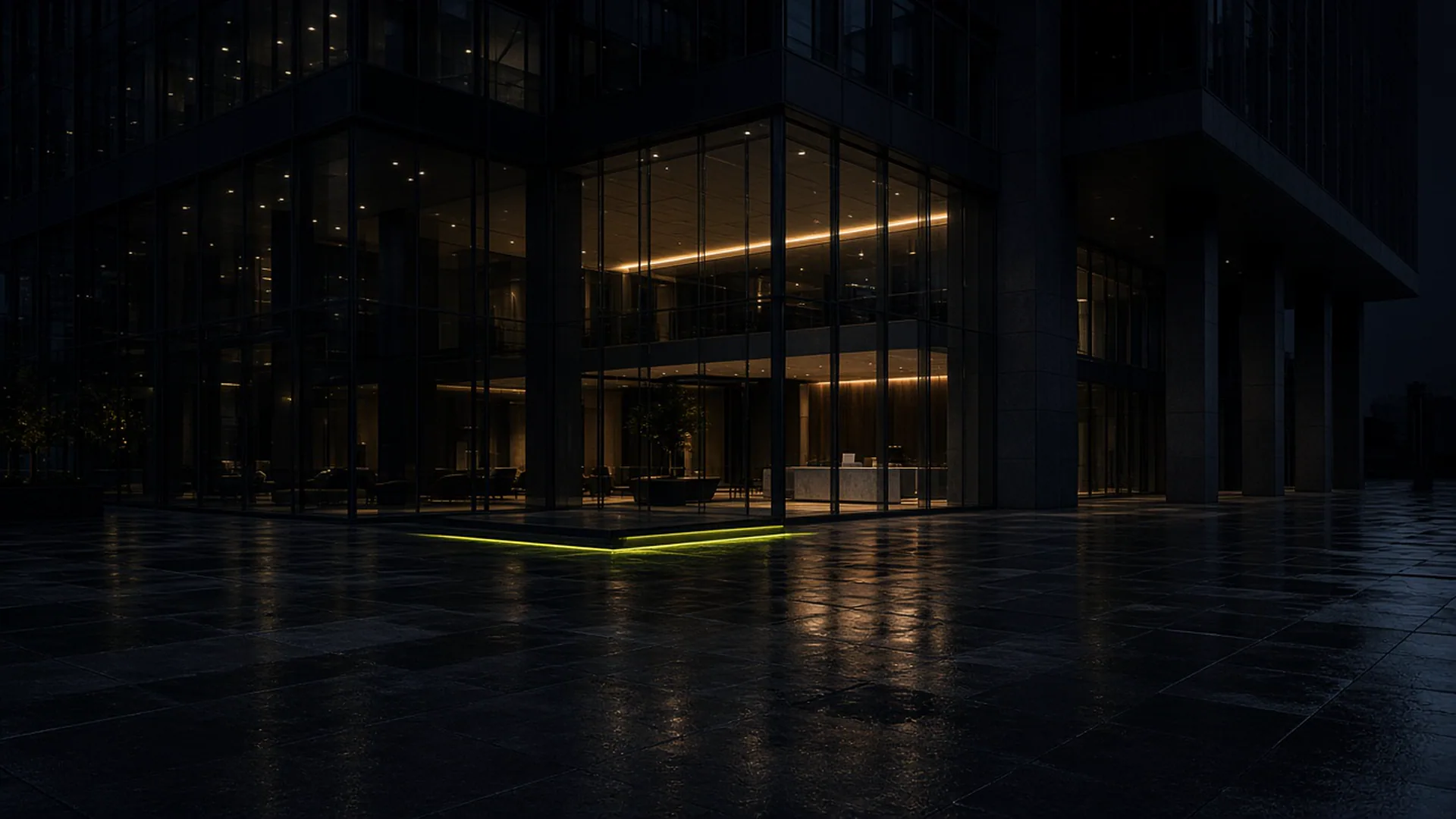 Night view of a glass office tower and wet plaza.