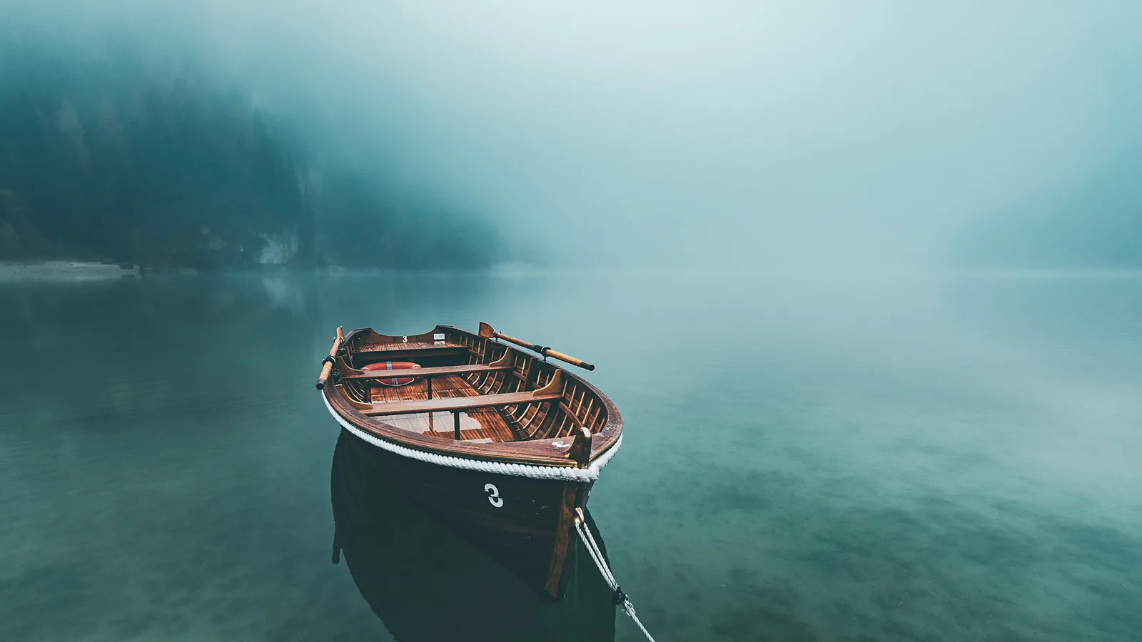 A wooden rowing boat moored on still teal water in mist
