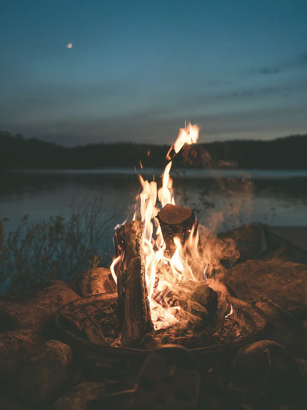 A fire burning on the shore at blue dusk, the loch behind it