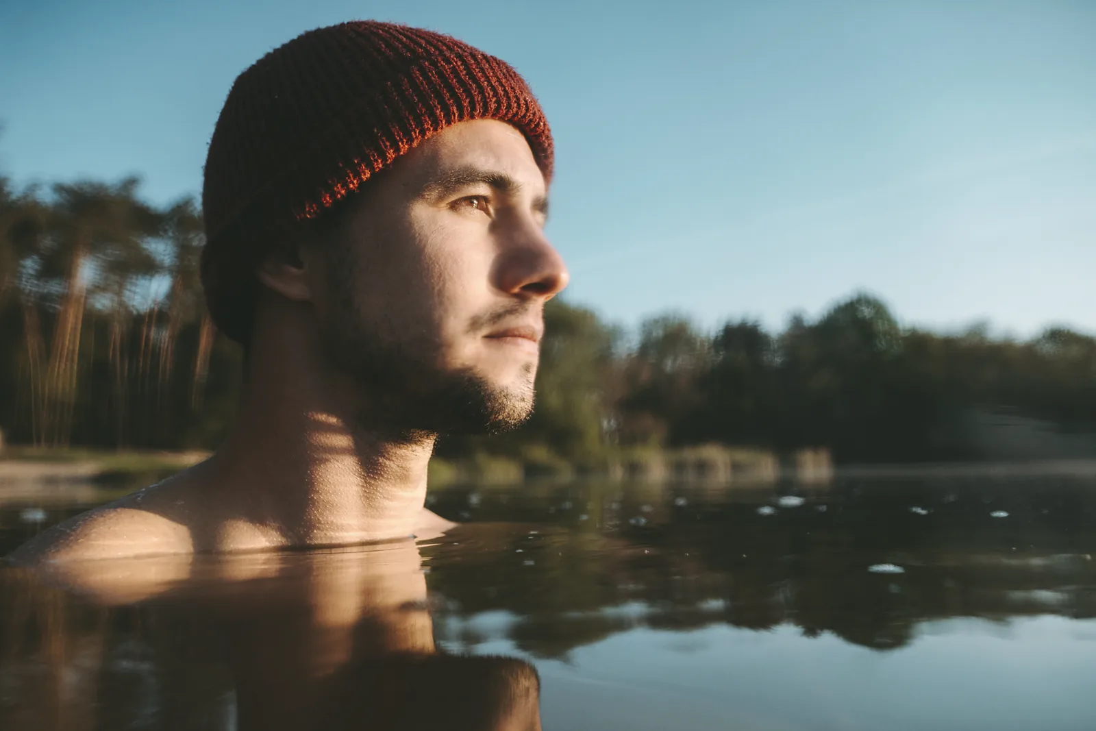 A man in a red wool hat swimming in the still loch at dawn