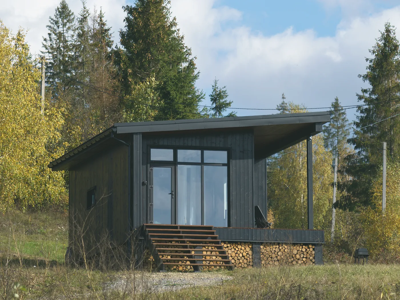 The Bothy: a compact charred-larch lodge with a glazed gable end, timber steps and a log store beneath the deck