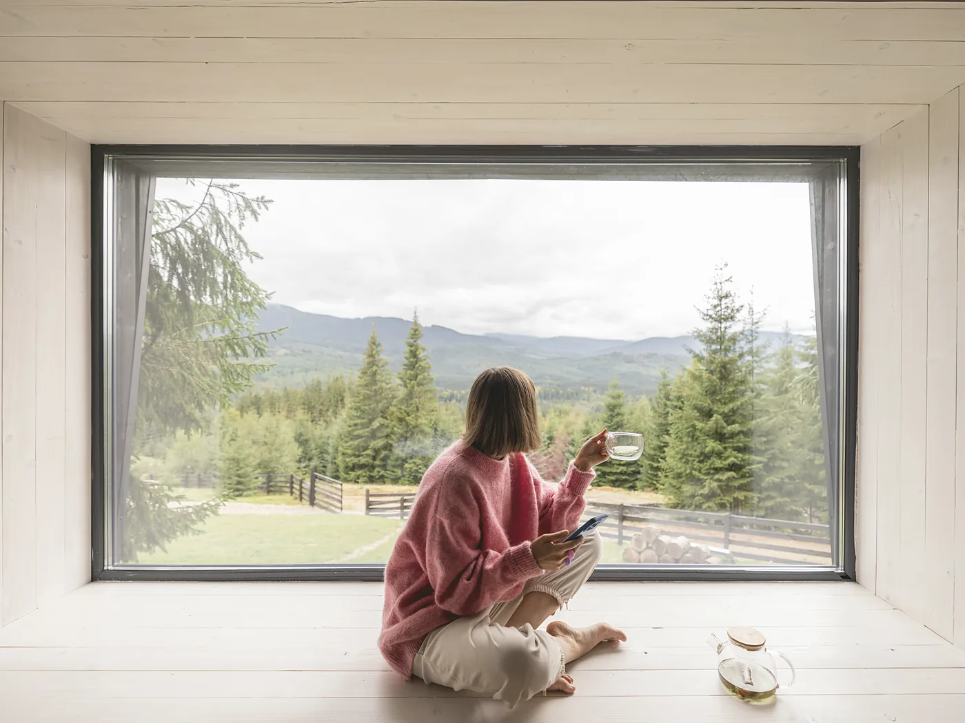 Inside a lodge: a deep picture window framed in pale pine, looking out over the tops of the trees