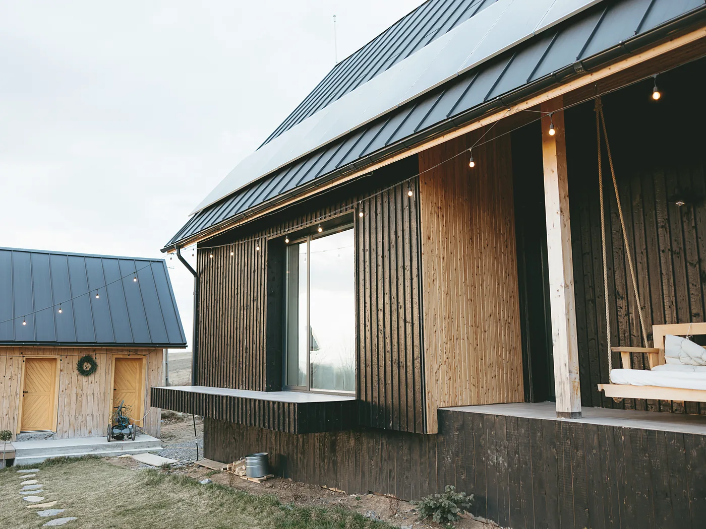 The Ridge: a two-storey lodge in natural and charred larch with a standing-seam roof, porch lights on at dusk