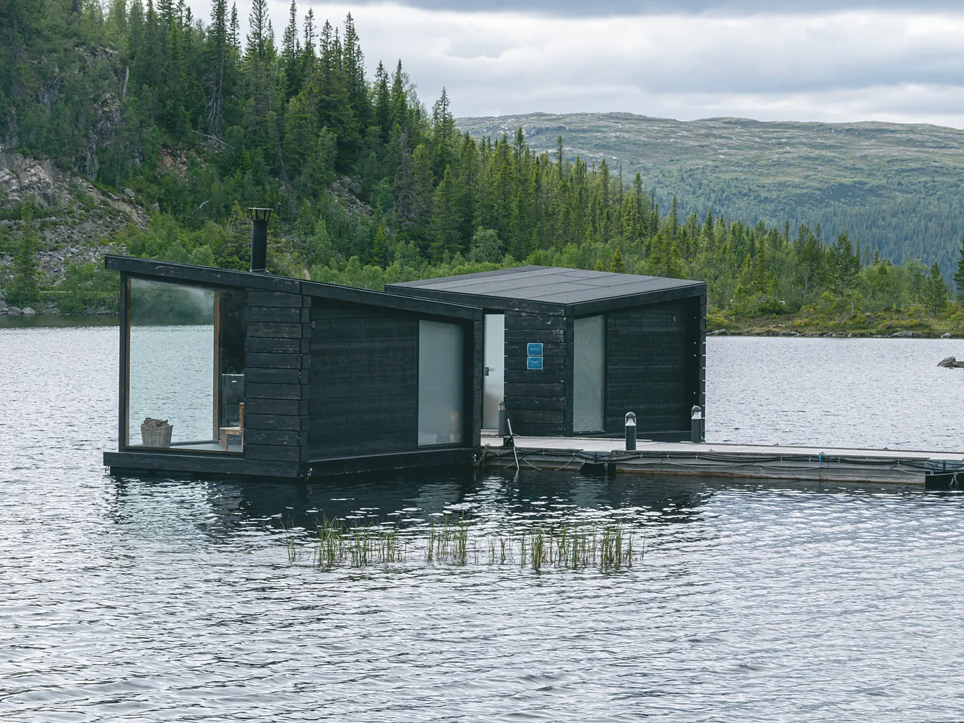 A charred-larch shore sauna moored at the loch edge on its own timber jetty