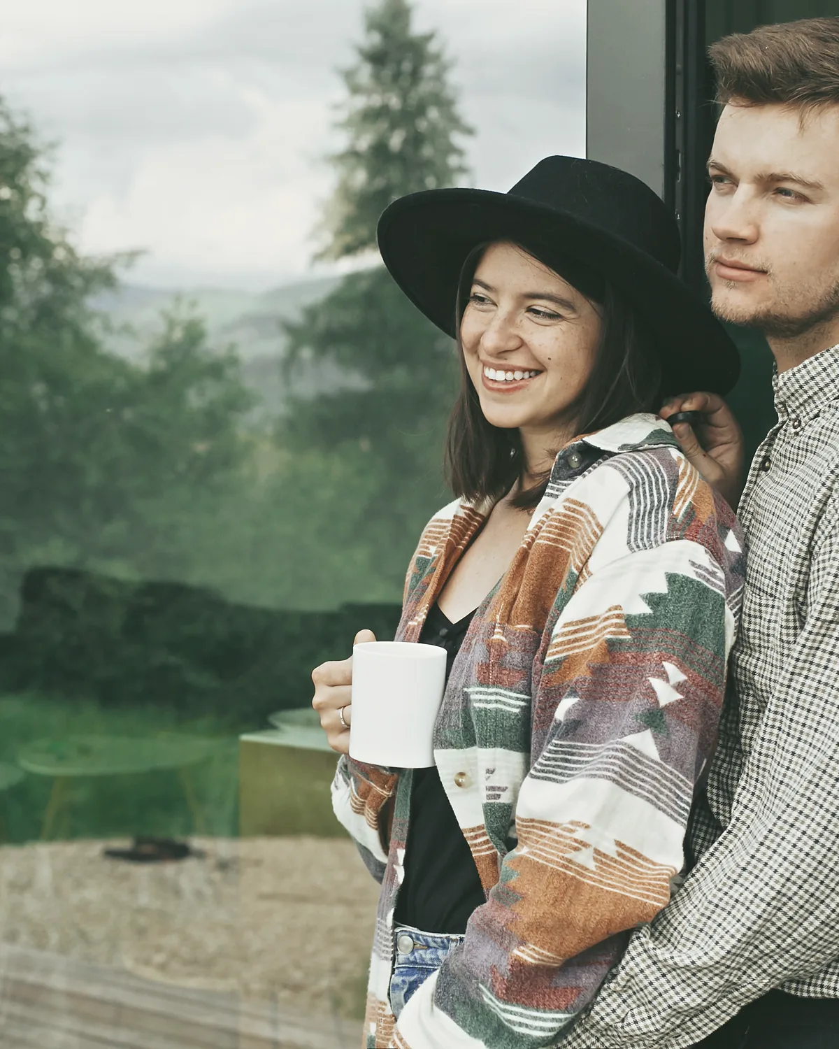 Two Phase 1 owners with coffee outside their lodge, the glass wall reflecting the wood behind them