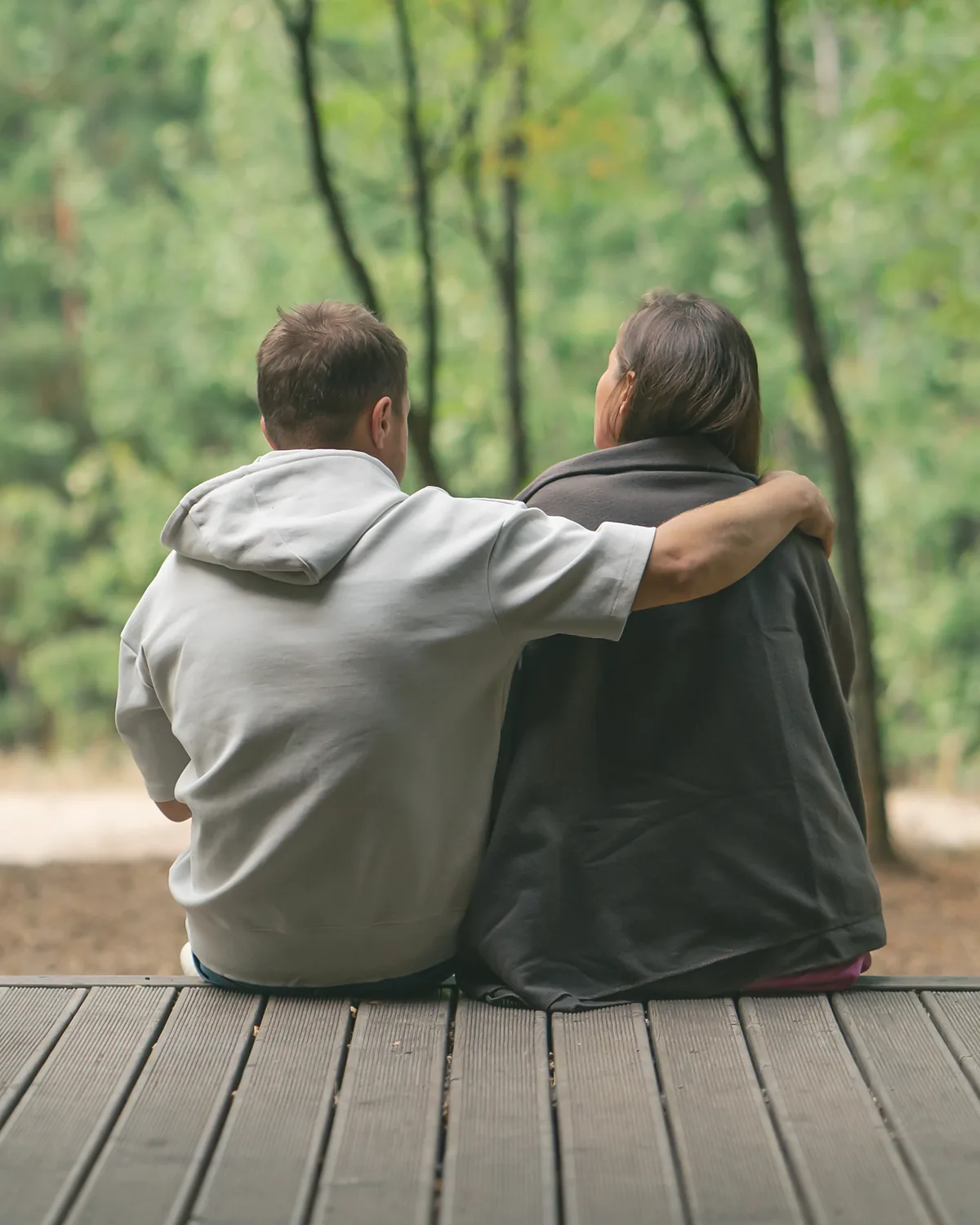 Two owners sitting on the deck of their lodge, looking out into the birch wood