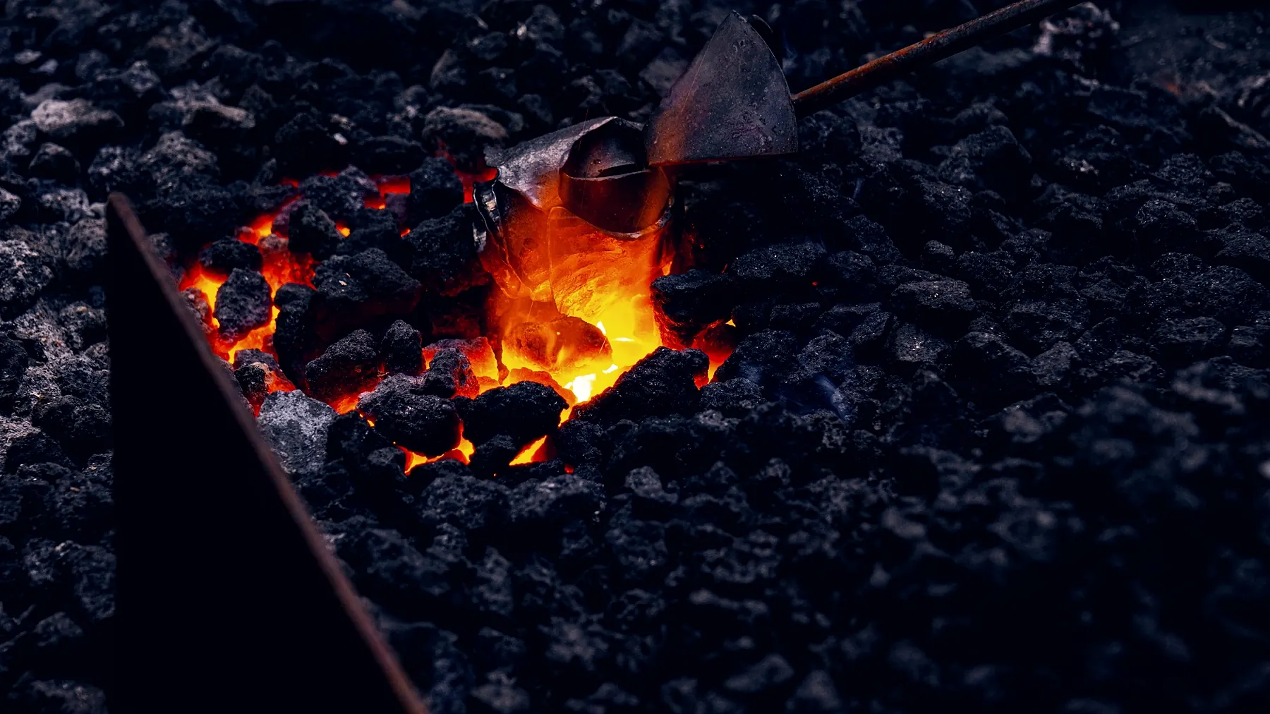 A billet of steel buried at welding heat in a bed of coal, the coals around it glowing dull red.