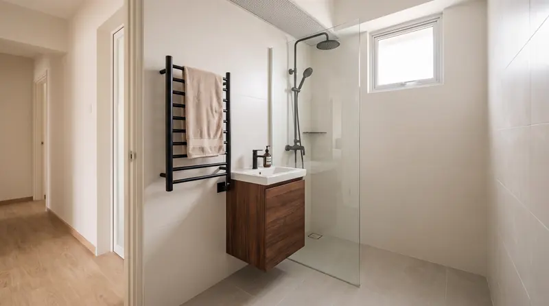 After: the common bathroom with large off-white wall tiles, a compact walnut vanity, a glass screen and matte black fittings.