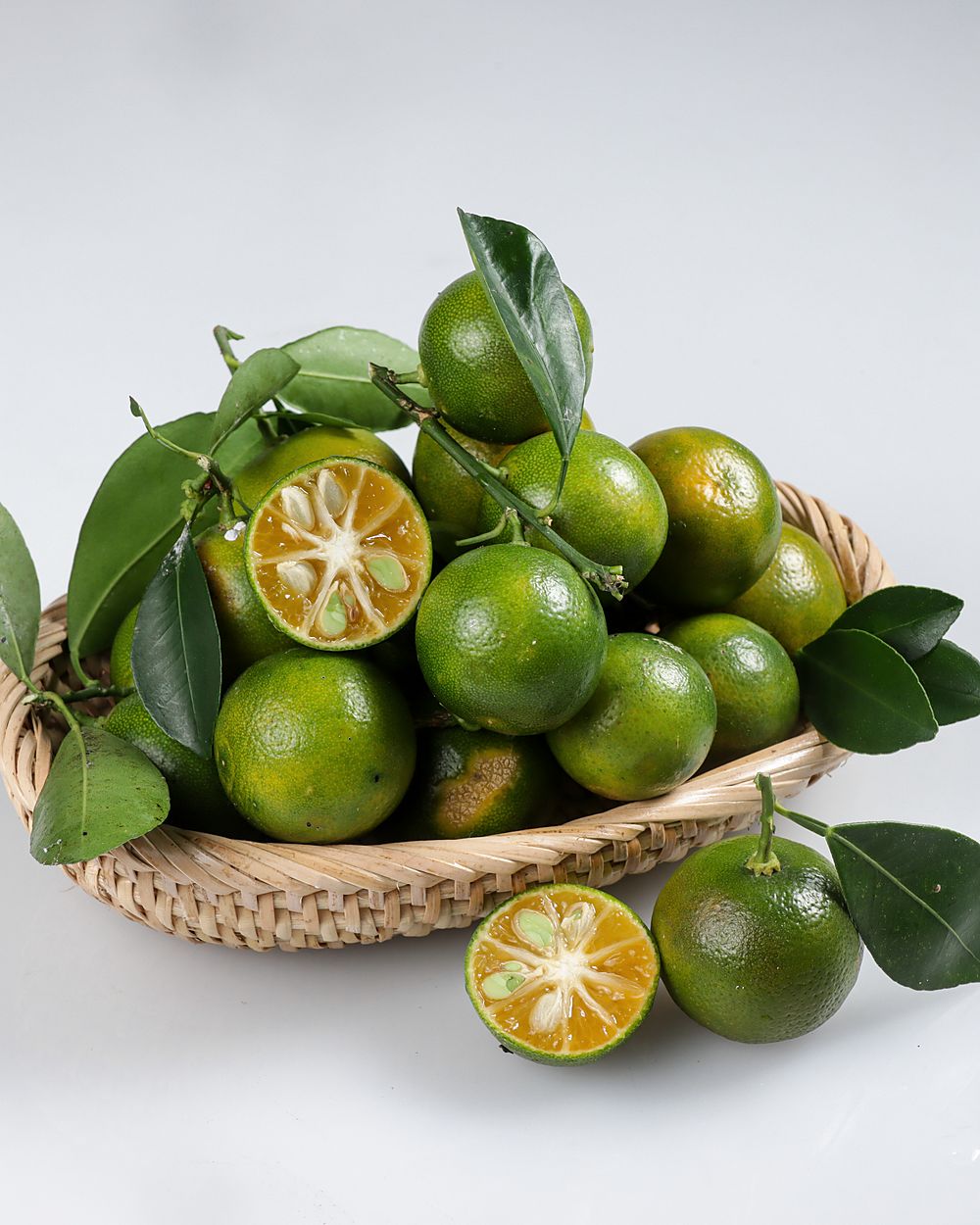 A basket of calamansi limes with their leaves, one cut open, on a grey table