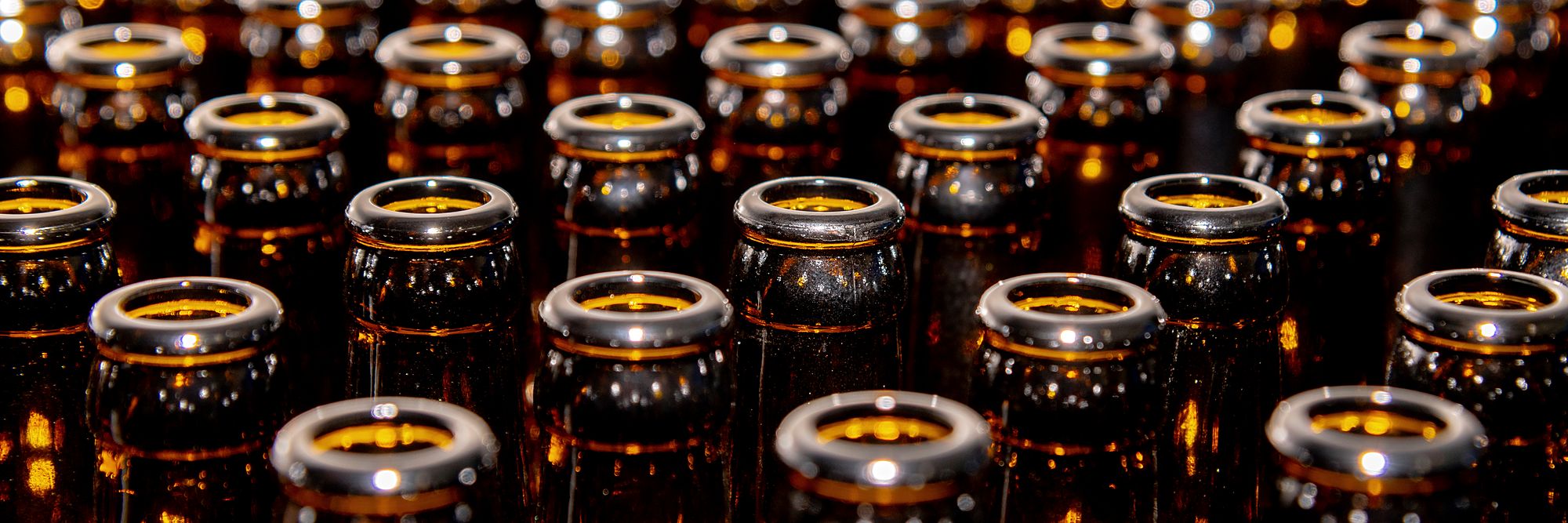 Rows of brown glass bottle necks with crown caps, seen from above, catching the light