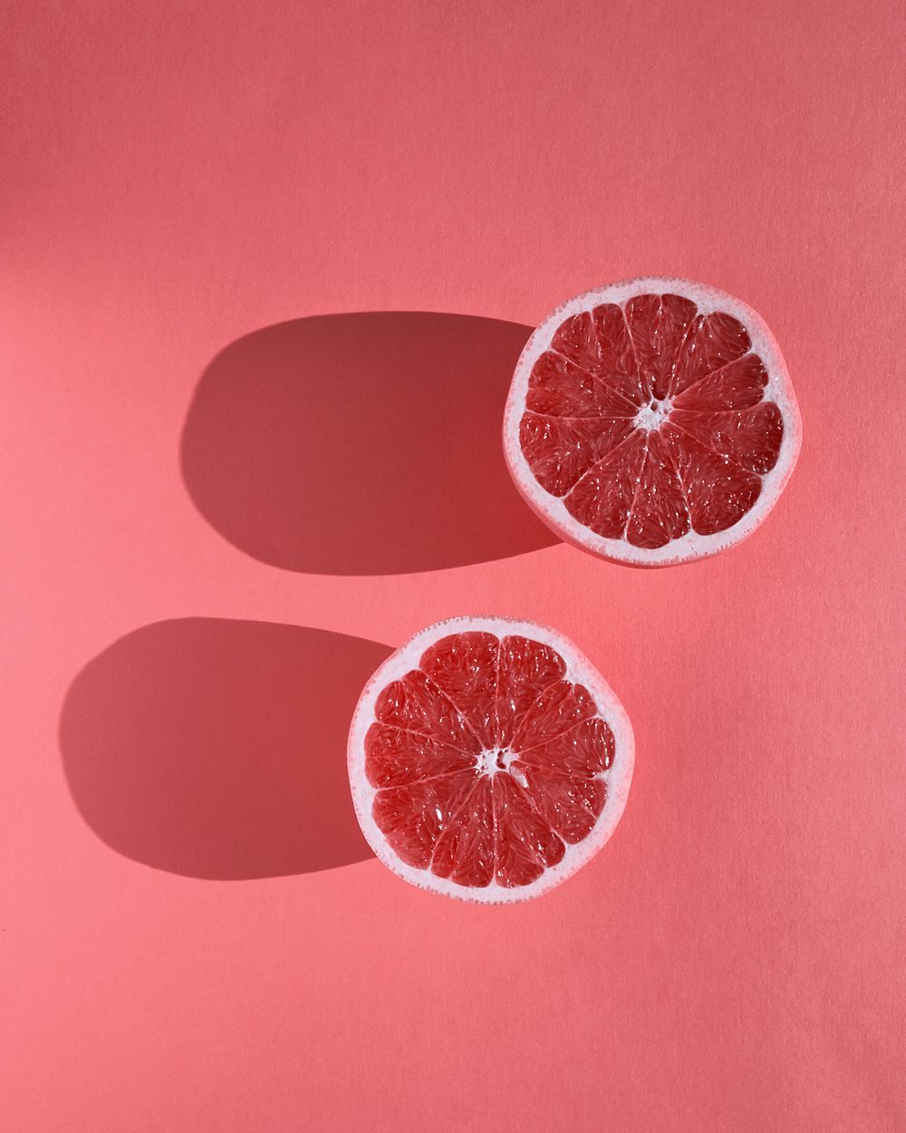 Two halves of a pink grapefruit on a soft pink background