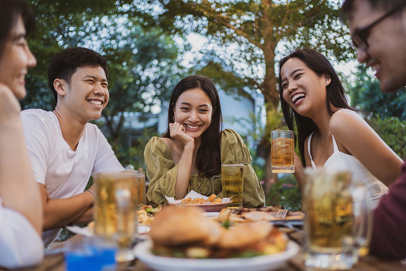 Four friends laughing around an outdoor dinner table, glasses of cold drinks in front of them