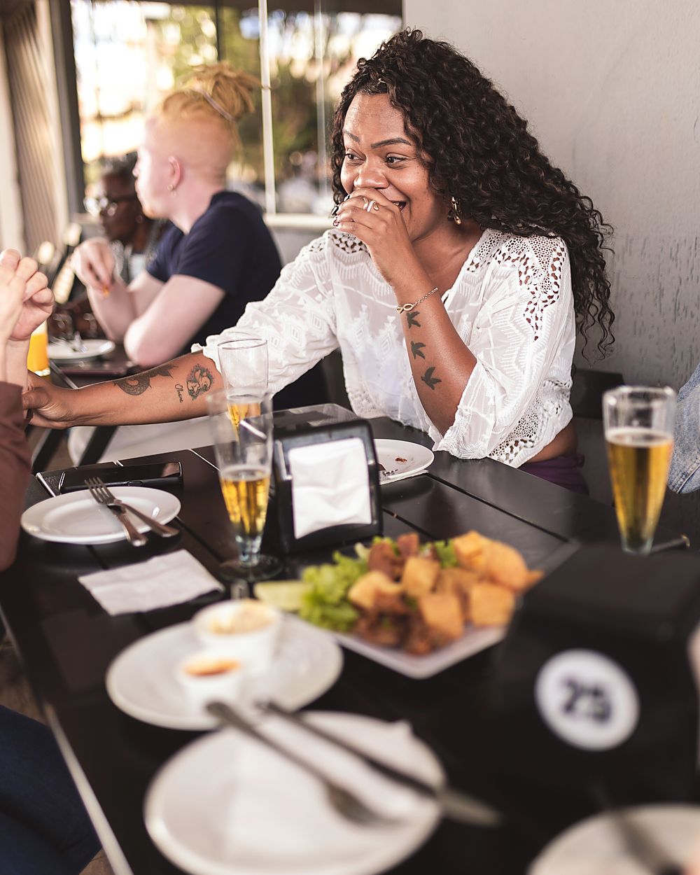 A woman at a restaurant table laughing with her hand over her mouth