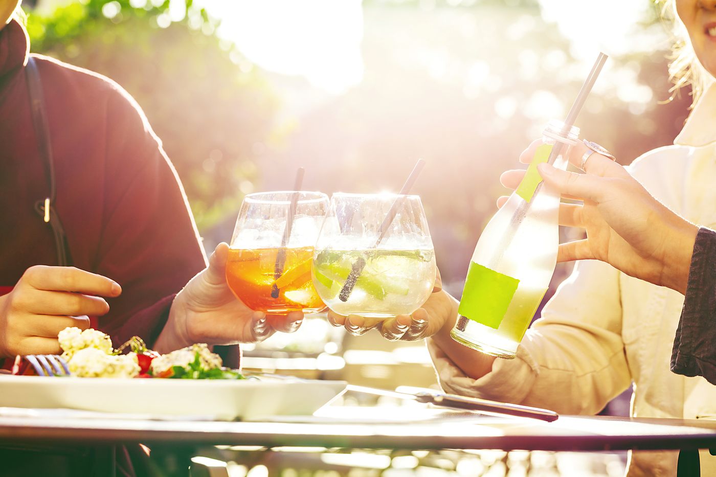 Friends clinking glasses over a lunch table in bright afternoon sun