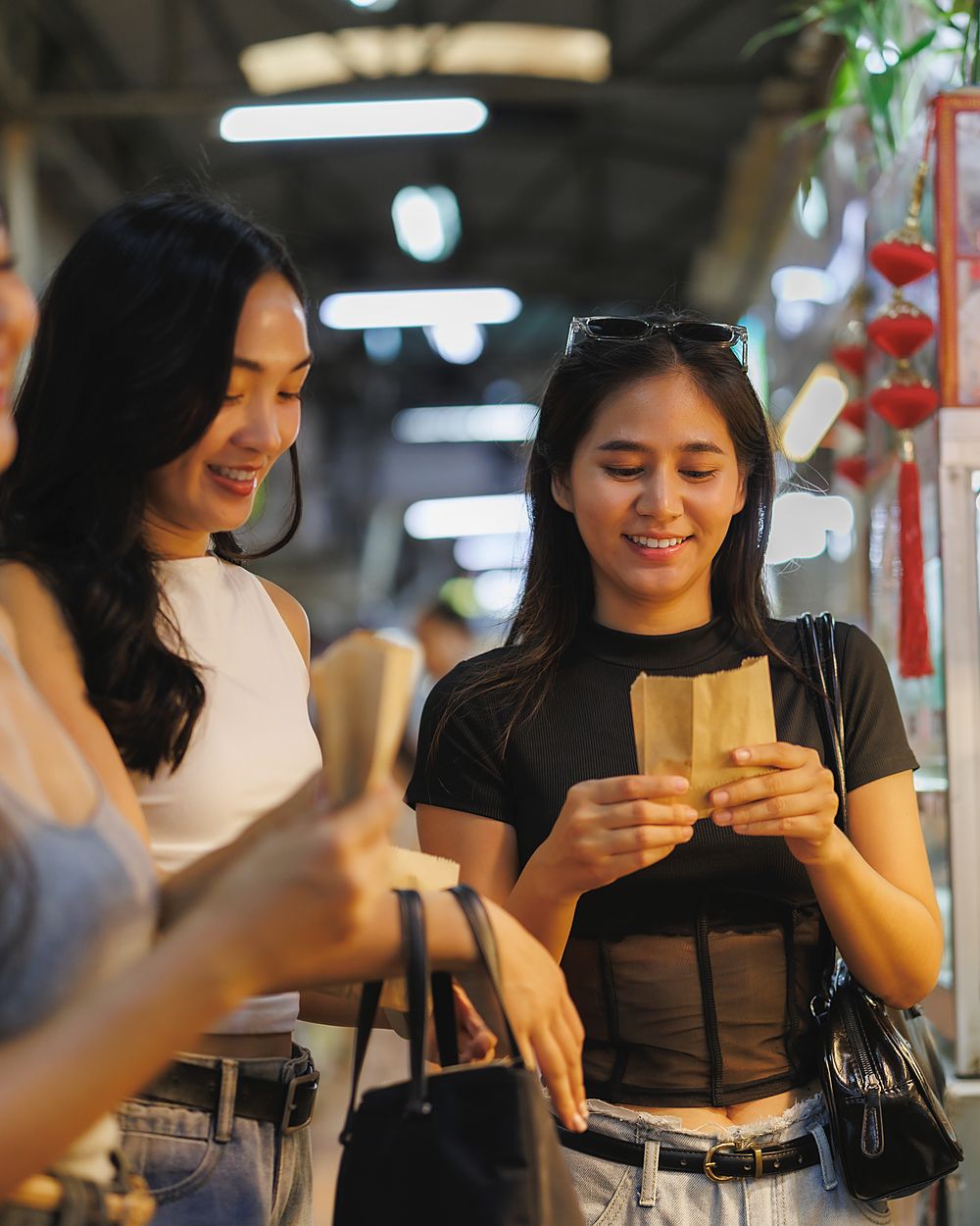 Three young women browsing a food stall under the lights of a covered market