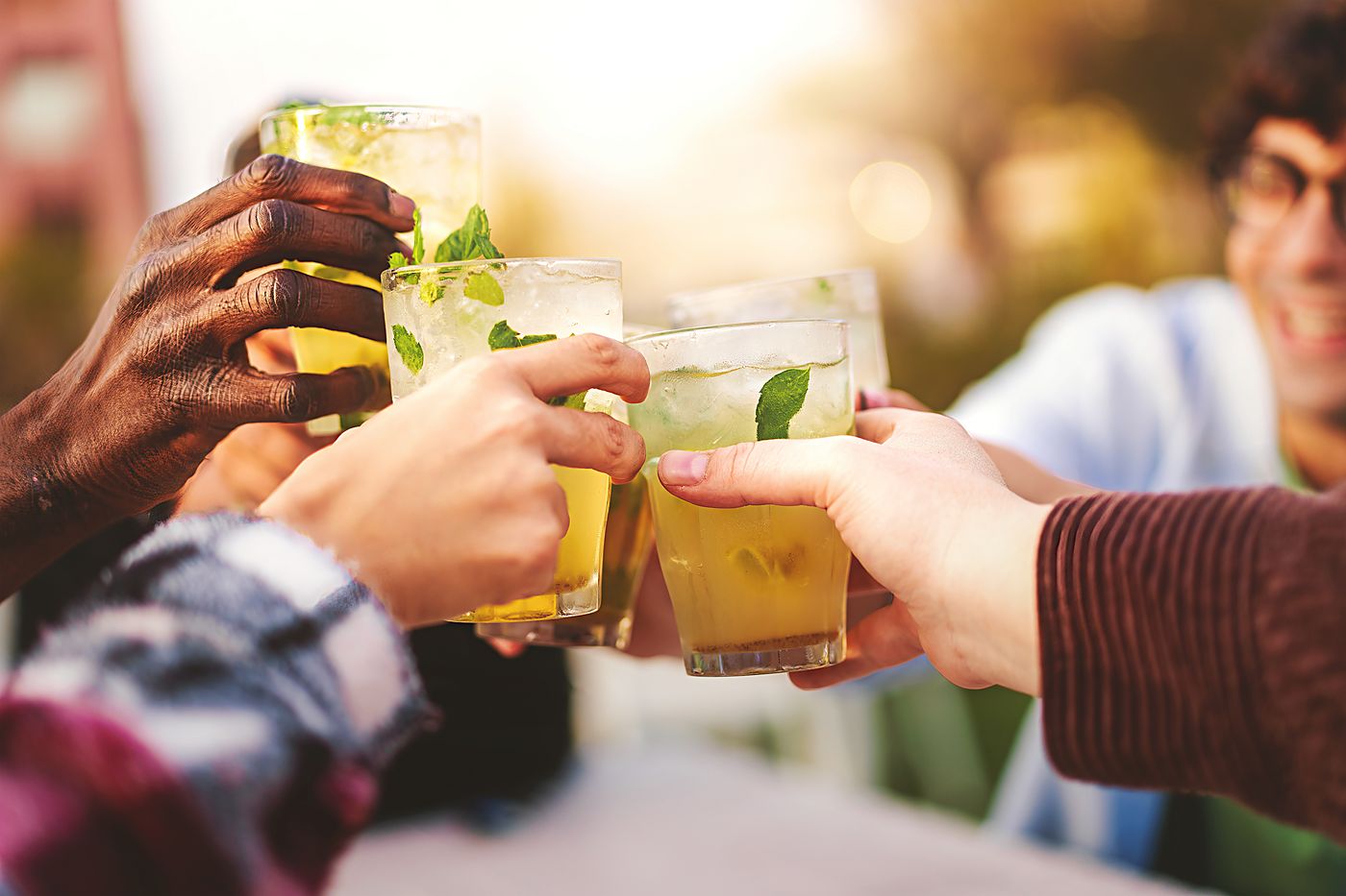 Hands clinking glasses of lime drink with mint and ice in low golden light