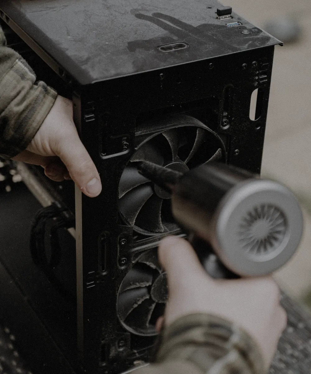 Hands holding an open case steady while an air blower clears dust from the fans.