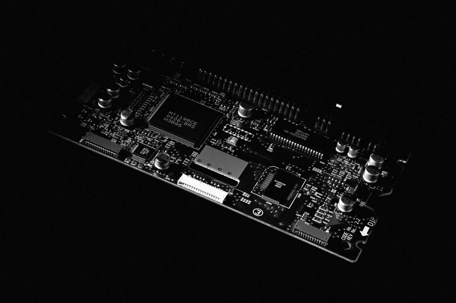 A bare circuit board with its chips and power components, lit from one side against black.