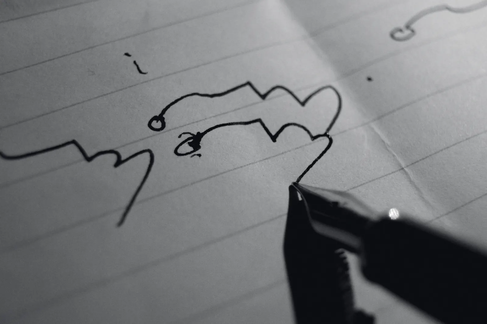 A steel nib drawing a looping line across lined paper, in black and white.