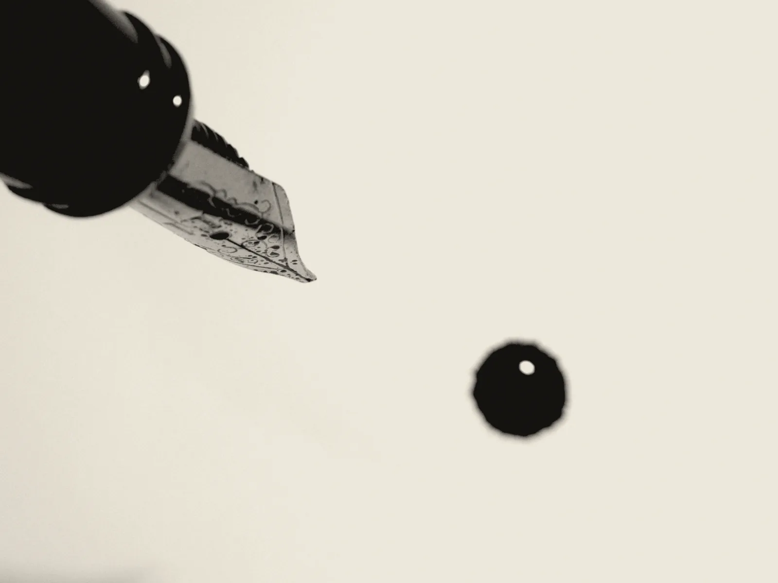A nib held above a sheet of paper and a single fallen drop of ink, high key.