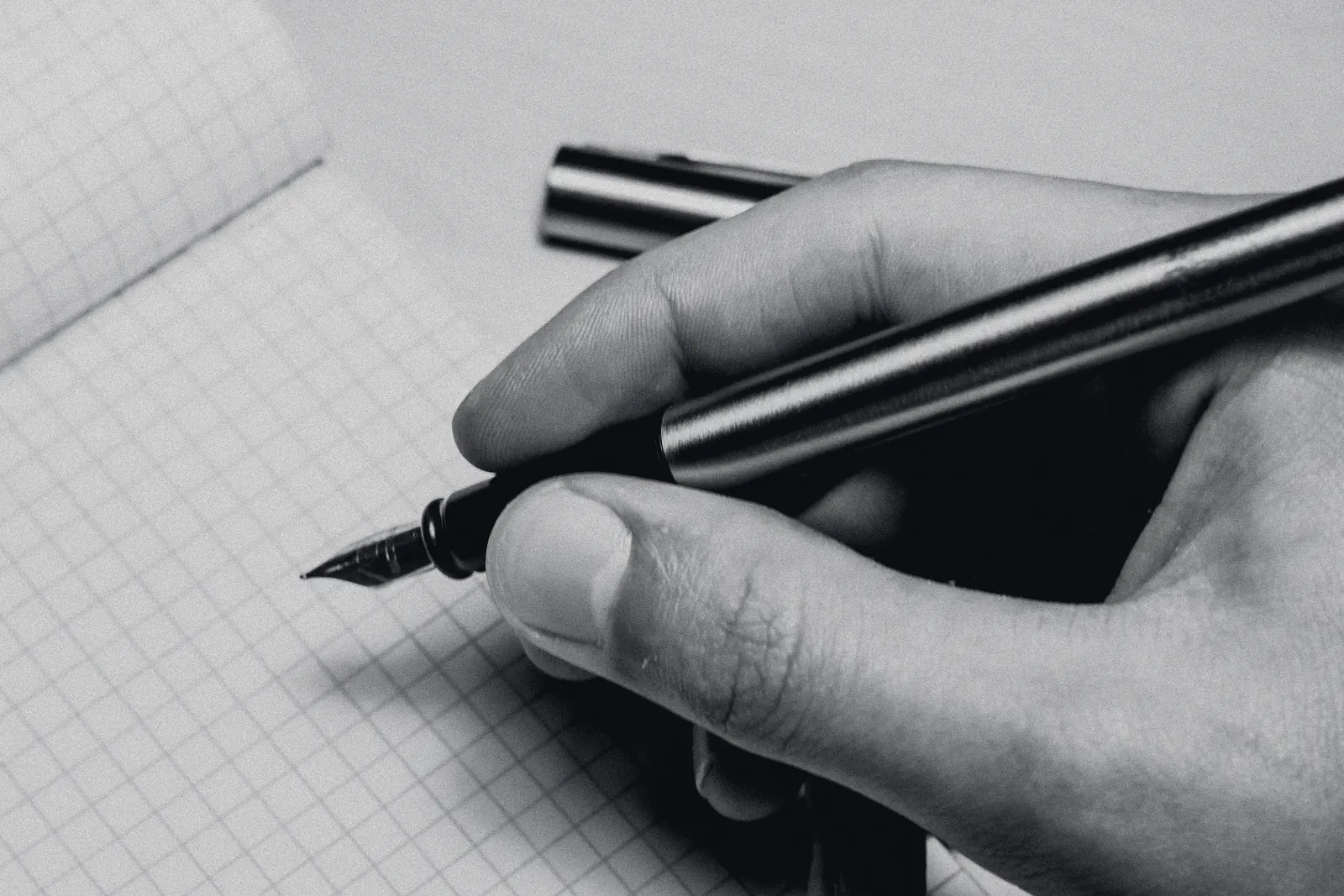 A hand holding a steel pen over grid paper, about to write.