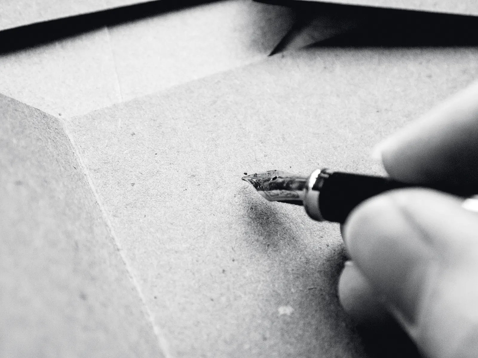 A hand writing on kraft paper with a steel-nibbed pen, close enough to see the tines.
