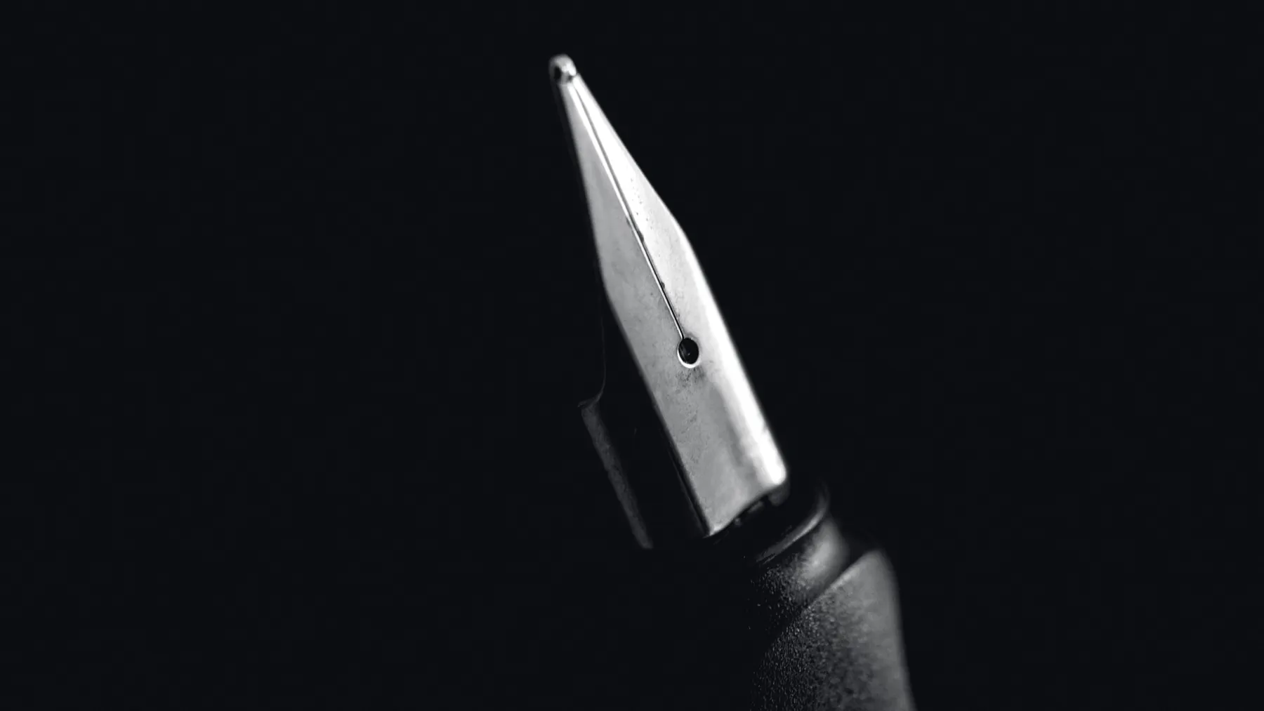 A steel nib filling the left of the frame against black: the slit, the breather hole and the ground ball of tipping at the point, in black and white.