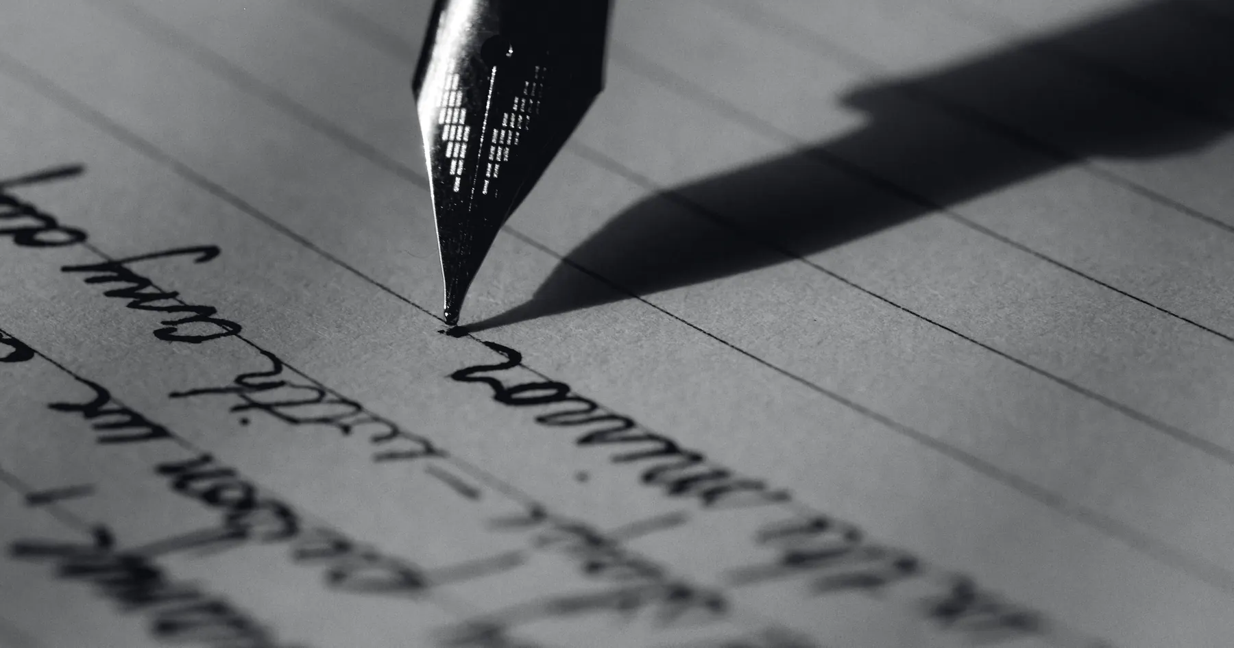 A steel nib on the line of a handwritten page, the tines and slit in focus, the writing falling away beneath.