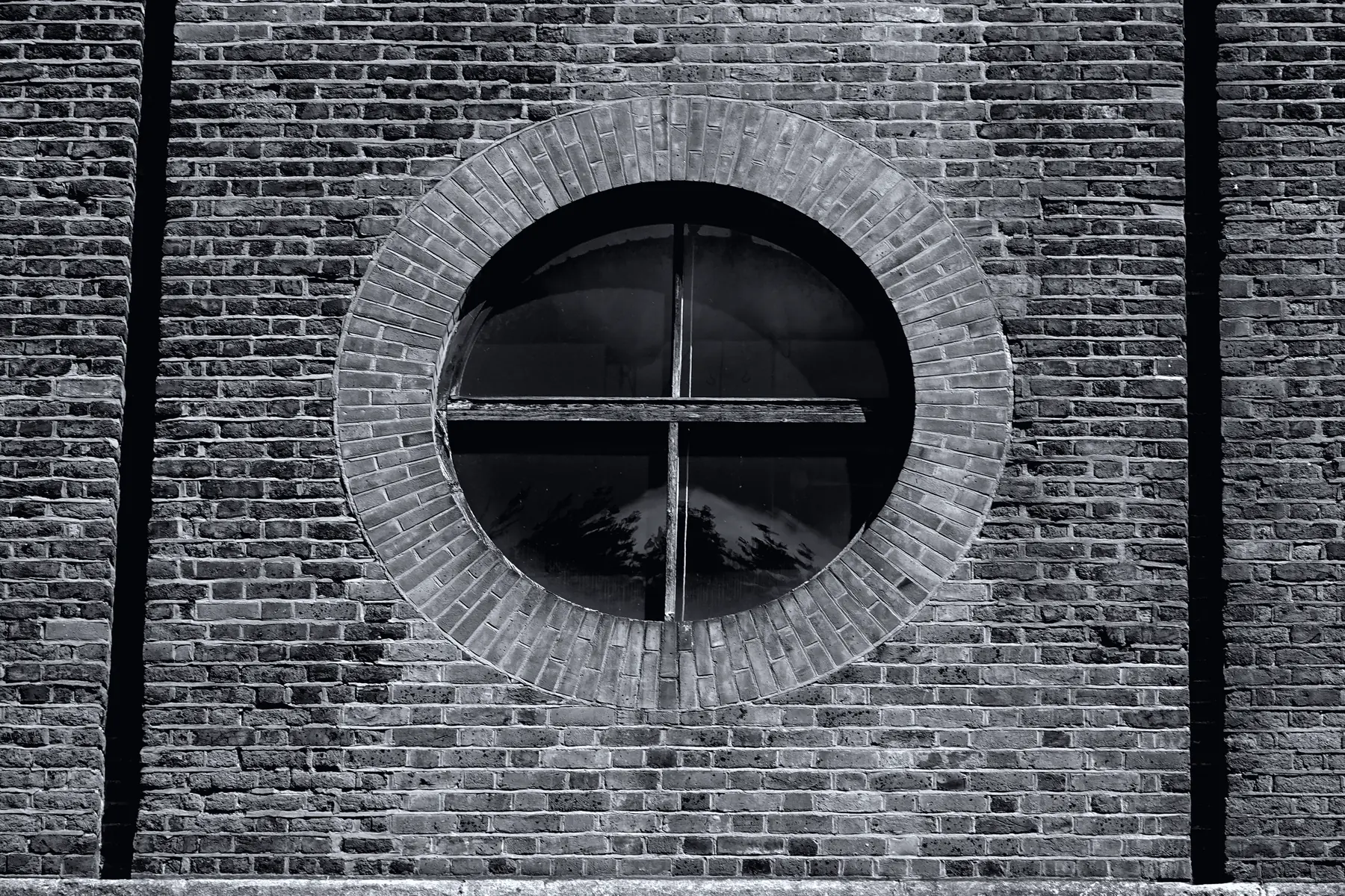 A round factory window set into a brick wall.
