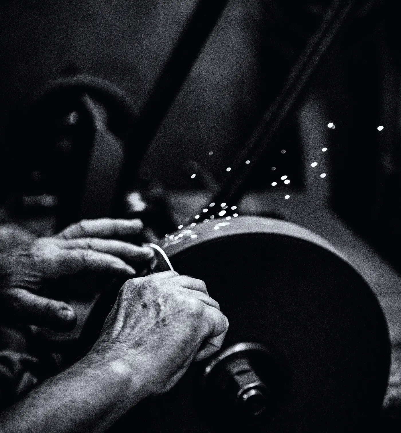 Hands working at a grinding wheel, a spray of sparks leaving the metal.