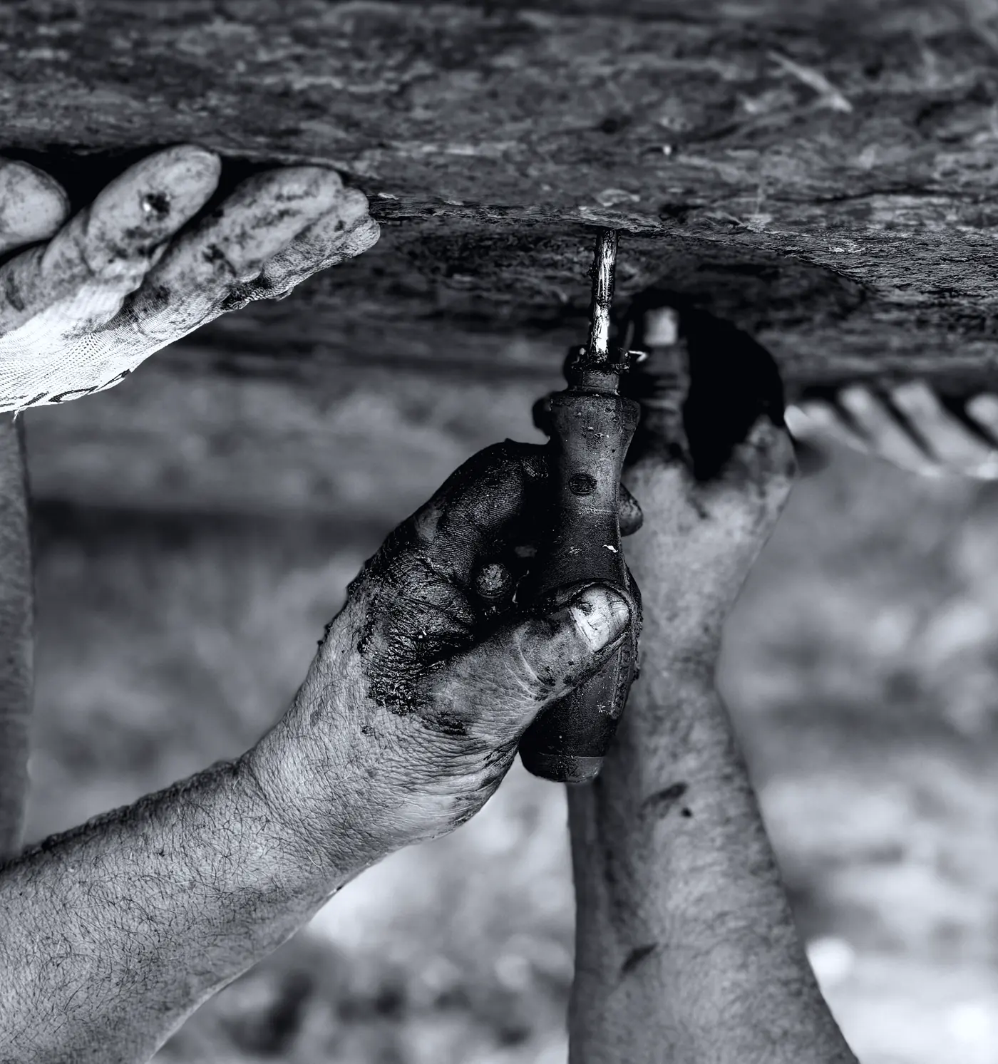 A pair of working hands, blackened at the knuckles, holding a steel tool.