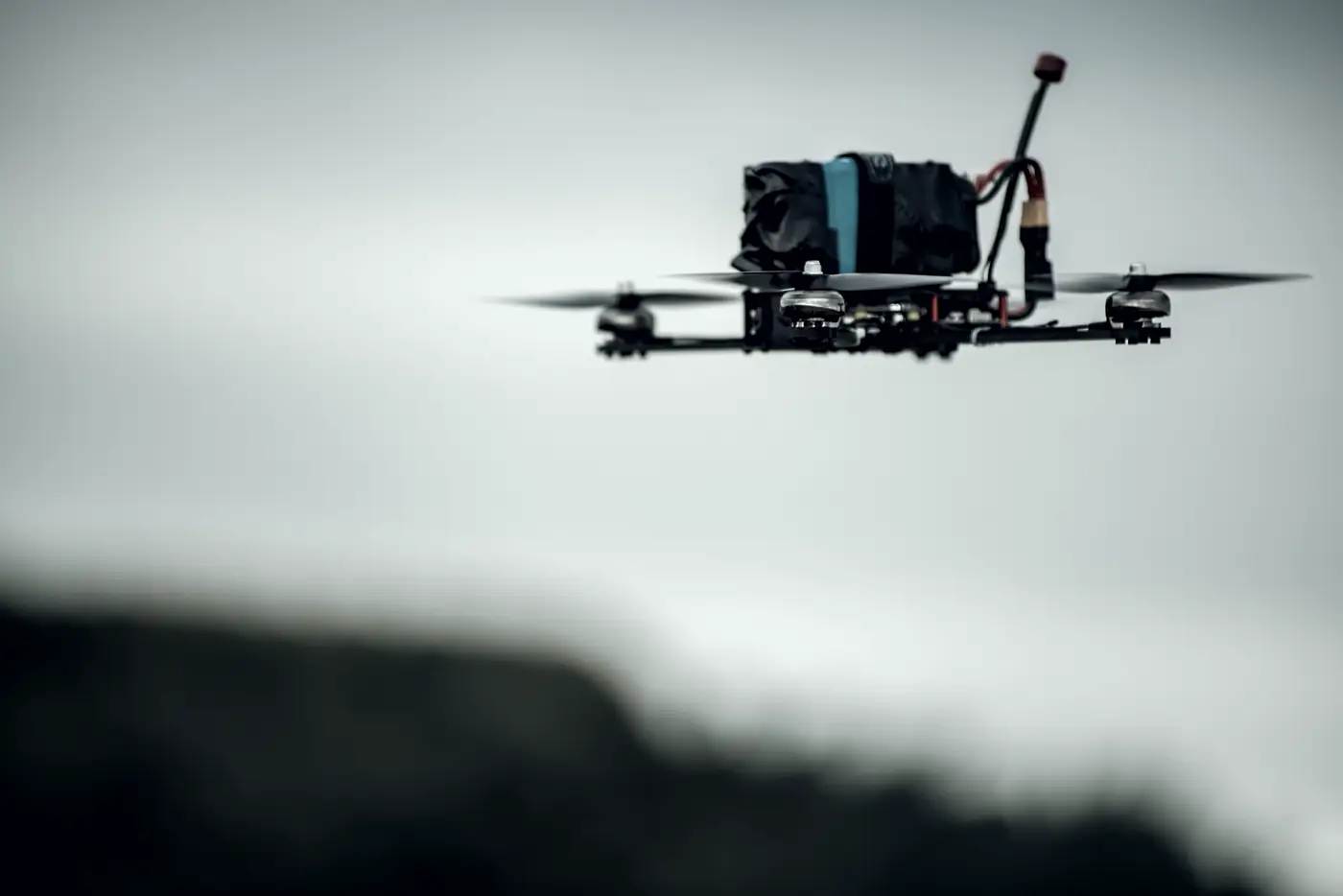 A racing quad in the air, side on, against a grey sky, its props a blur.