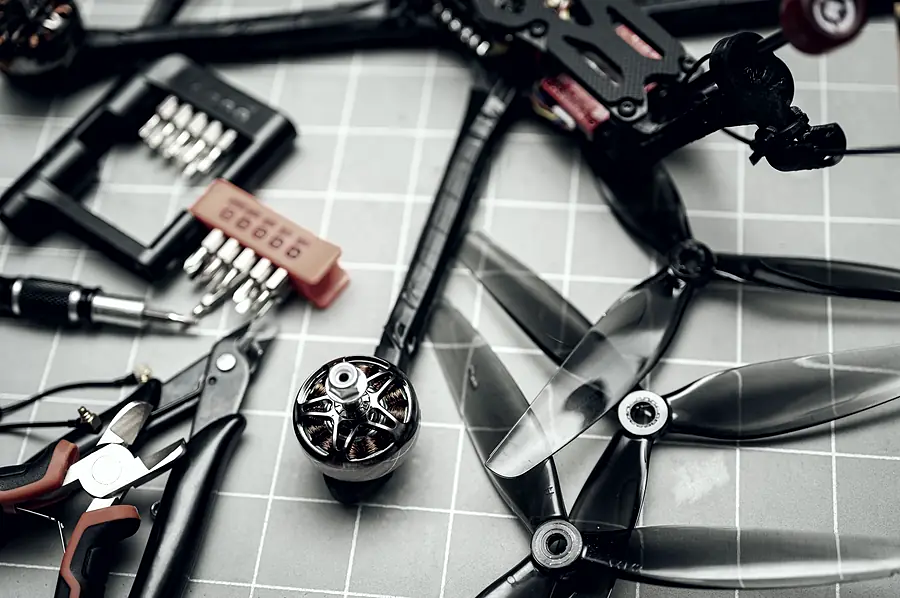 Props, a bare motor, a screwdriver set and side cutters on a cutting mat, next to a carbon racing frame.