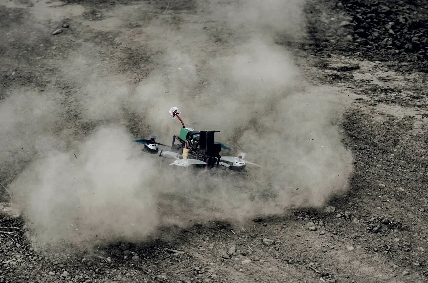 A racing quad lifting off a dirt track inside the cloud of dust its own props have thrown up.