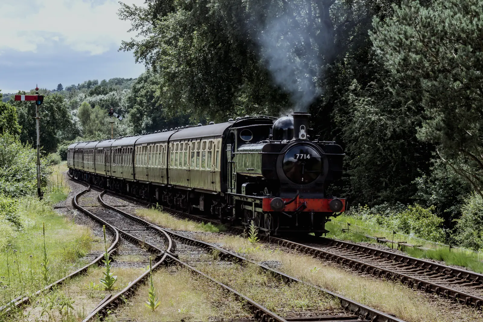 A tank engine and four carriages running towards the junction on a summer afternoon, a semaphore signal standing at danger on the left and a set of points in the foreground.