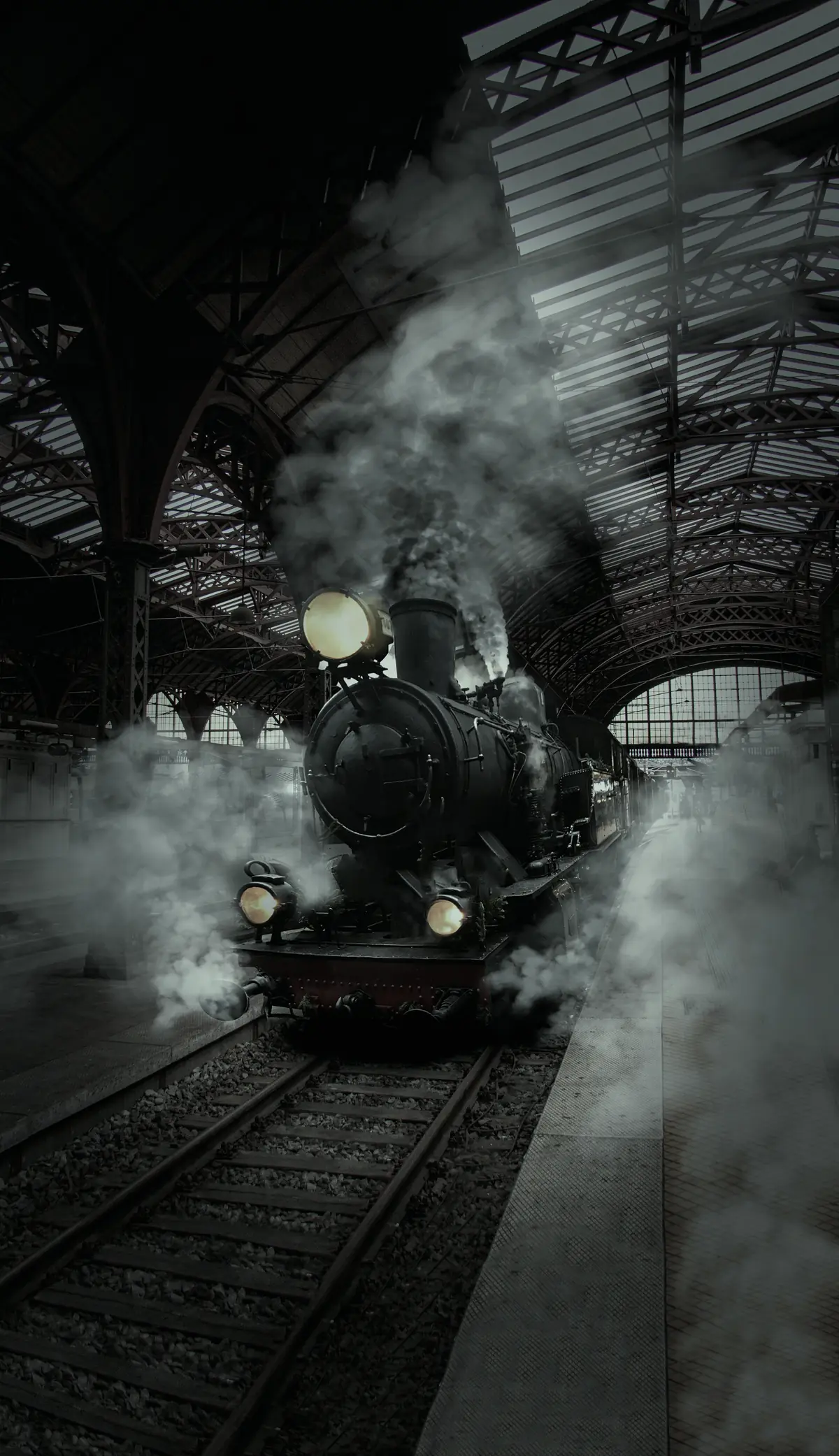 A locomotive standing under a station roof at night, lamps lit, steam drifting across the platform.